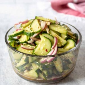 A glass bowl filled with cucumbers and onions.