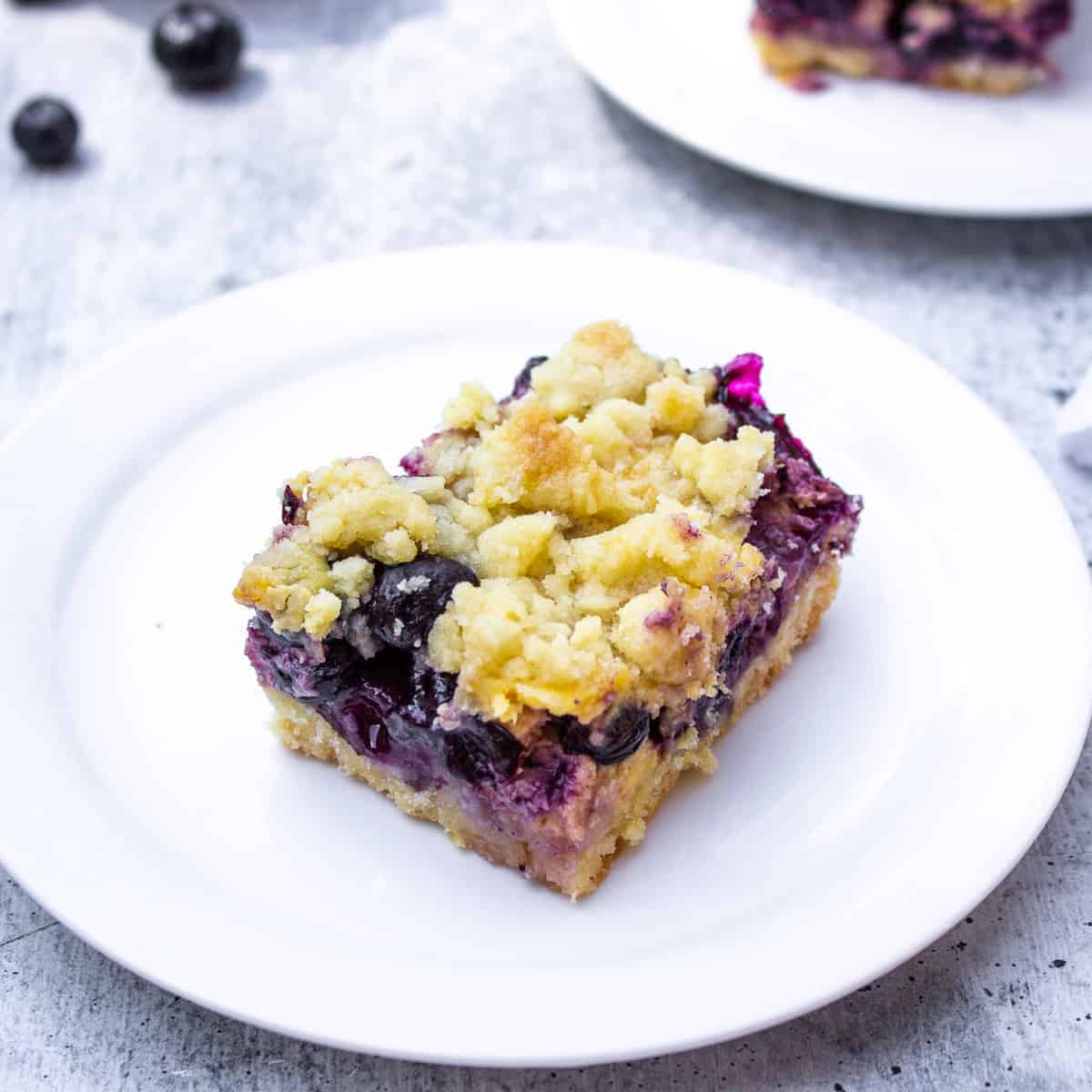 A square cut dessert filled with blueberries and topped with a crumb topping.