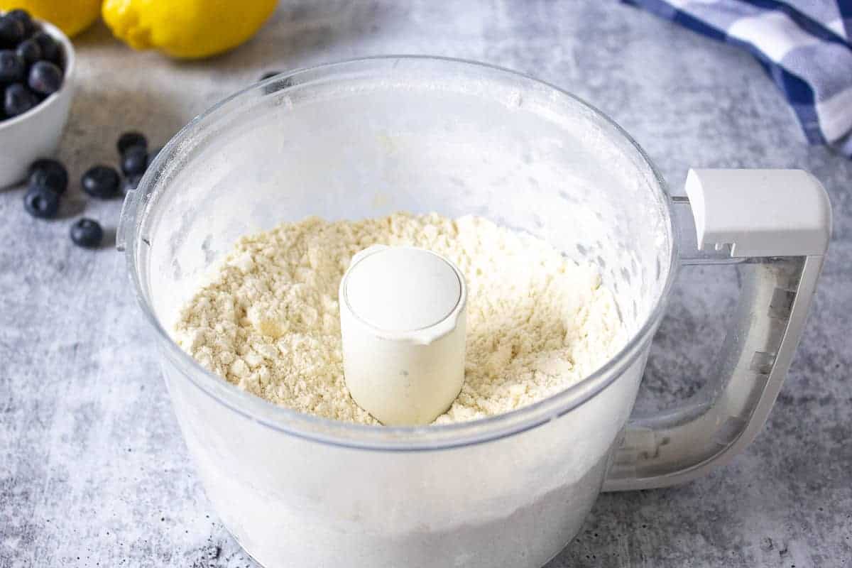 Crumbly flour mixture in a food processor bowl.