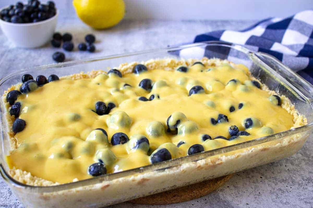 Lemon filling poured over blueberries in a glass casserole dish.