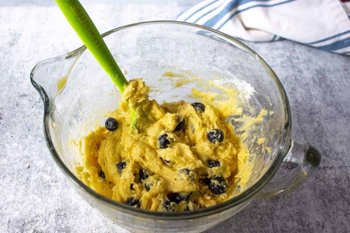 Blueberry lemon batter in a glass bowl with a green spatula.