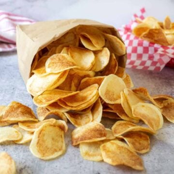Homemade potato chips spilling out of a brown paper bag.