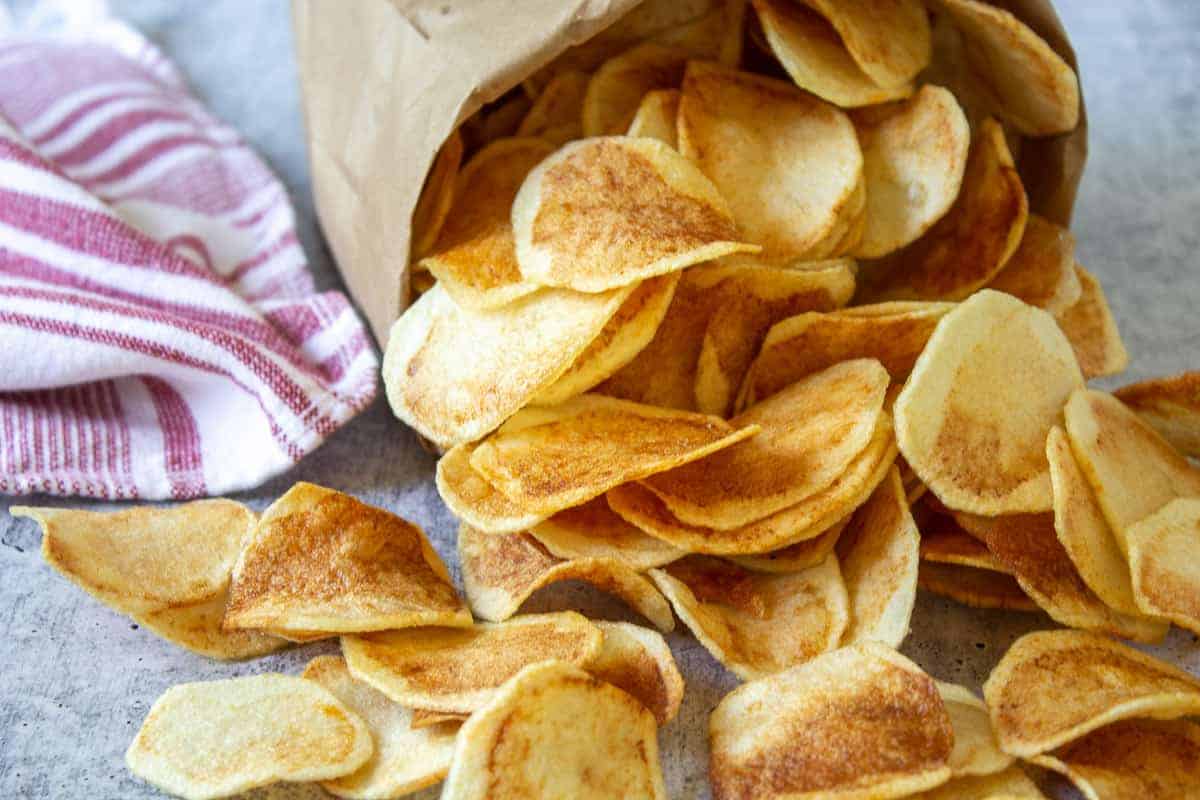 Homemade potato chips spilling out of a brown paper bag. 