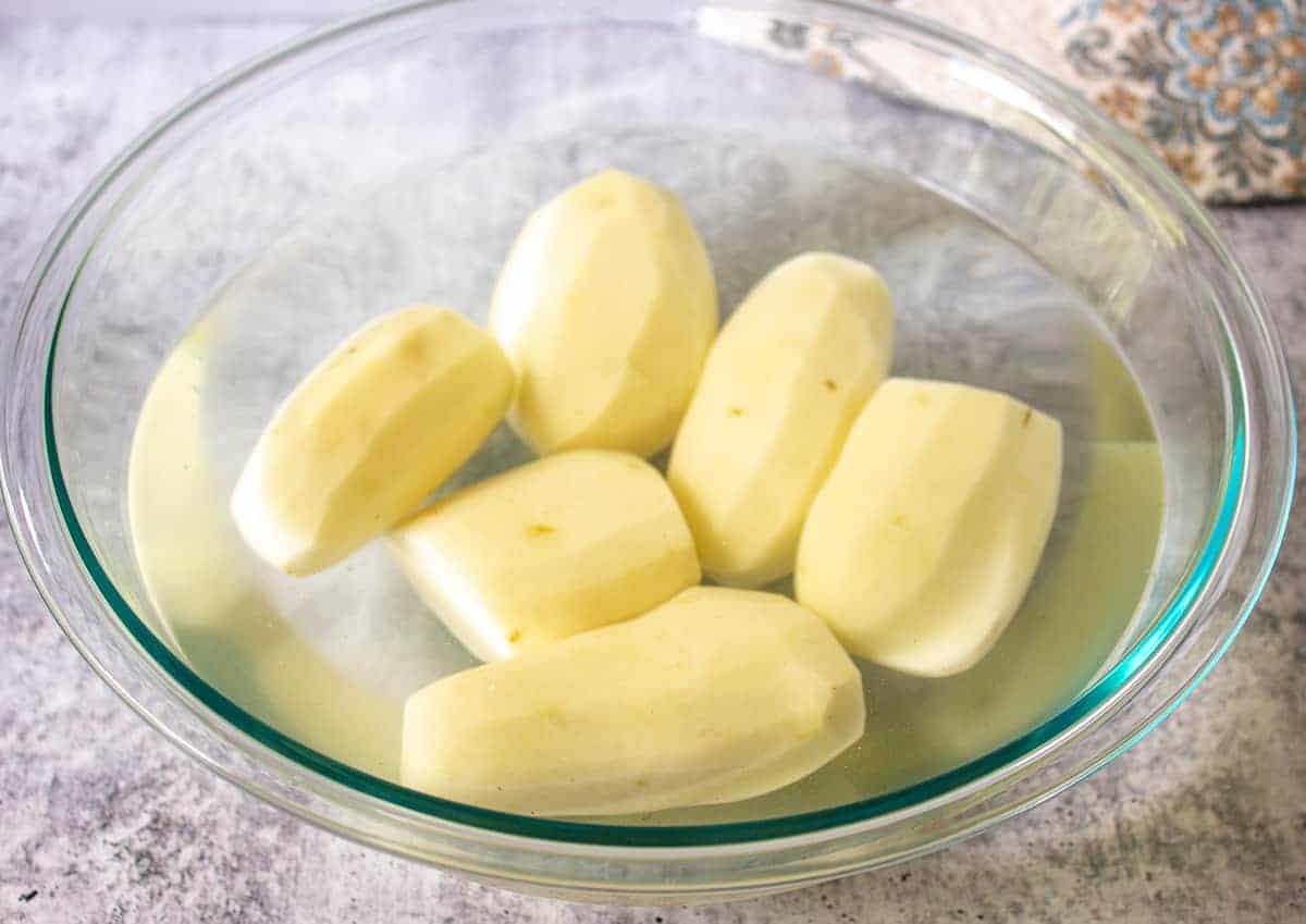 Peeled potatoes in a glass bowl.