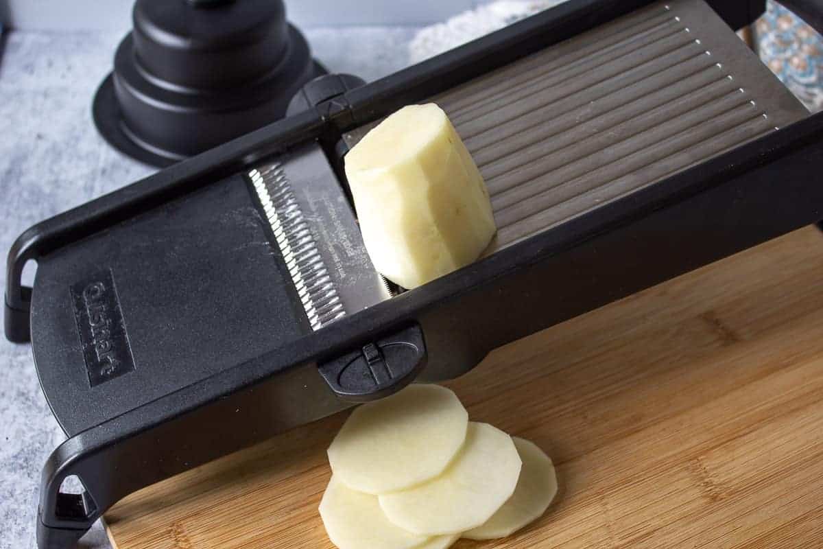 Potatoes being sliced on a mandoline.