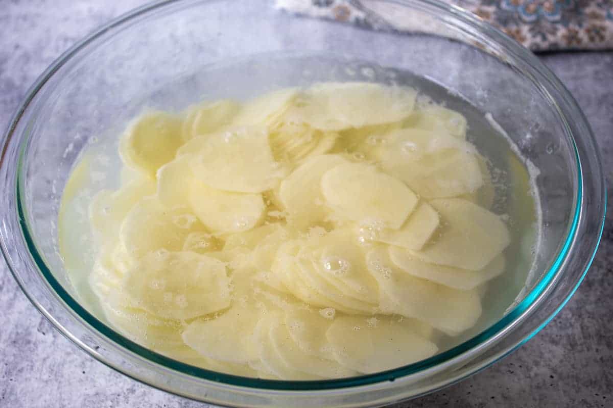 Potato slices soaking in a bowl of water.