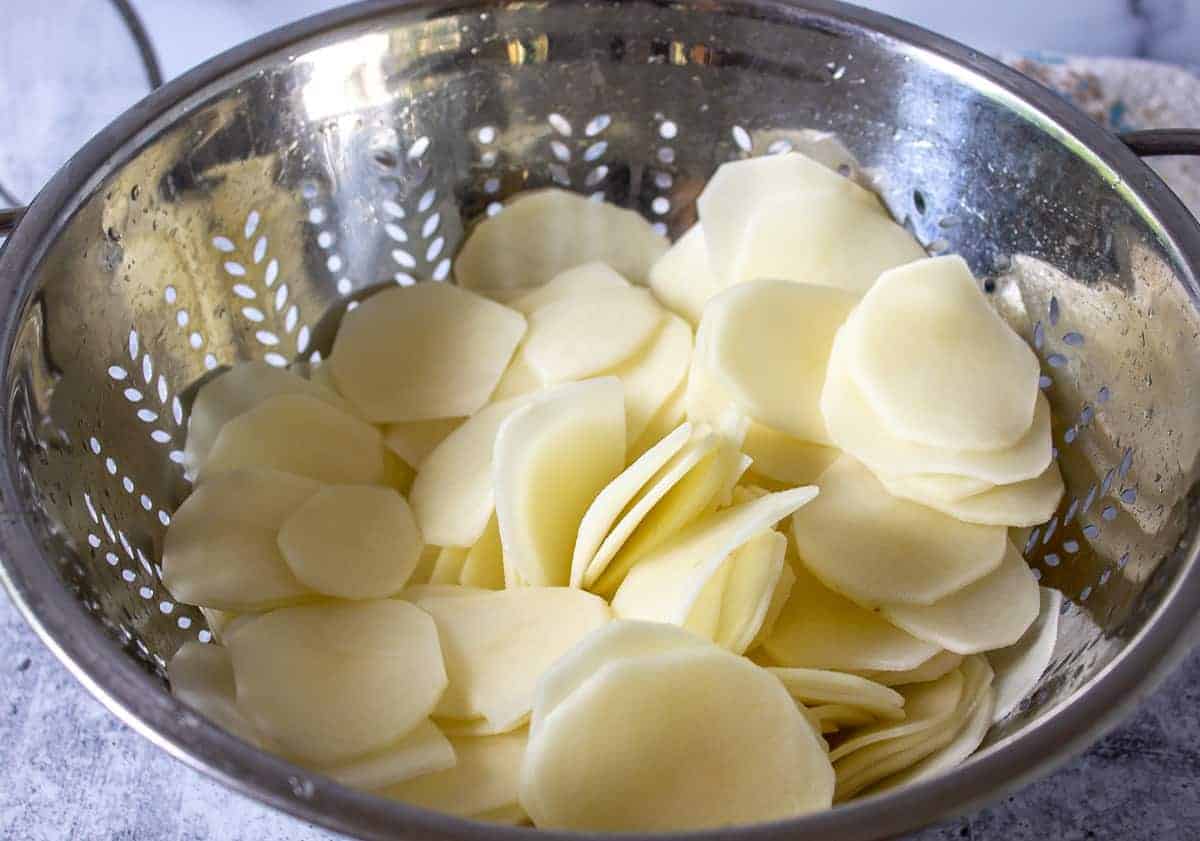 Potato slices in a metal colander.