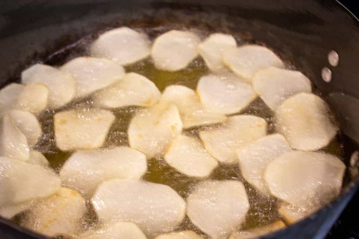 Potato chips frying in a pot of hot oil.