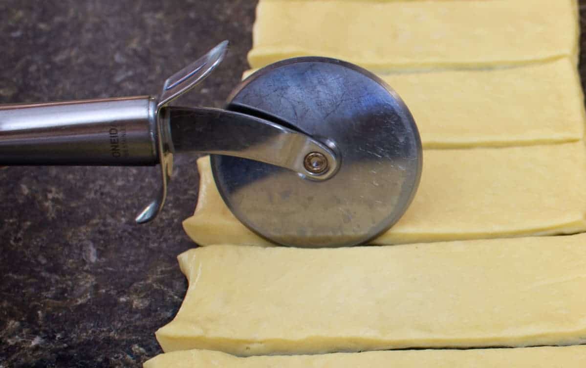 Slicing dough into smaller rectangles with a pizza slicer.