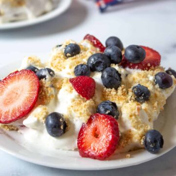 A plate full of whipped cream with fresh strawberries and blueberries.