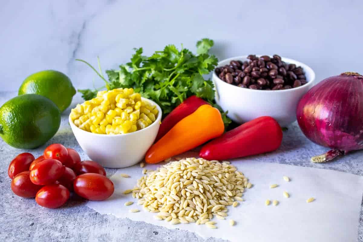 An arrangement of ingredients, including orzo, tomatoes, corn, black beans, bell peppers, cilantro and a red onion.