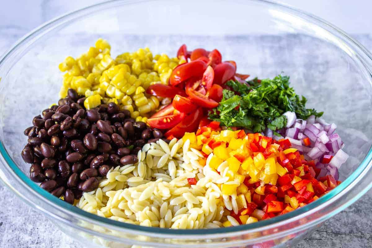 A glass bowl filled with freshly cut veggies, black beans and orzo pasta.