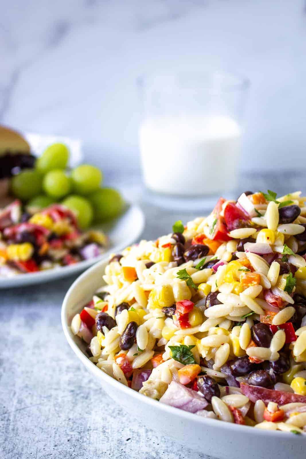 Orzo pasta on a table with a plate filled with food and a glass of milk. 