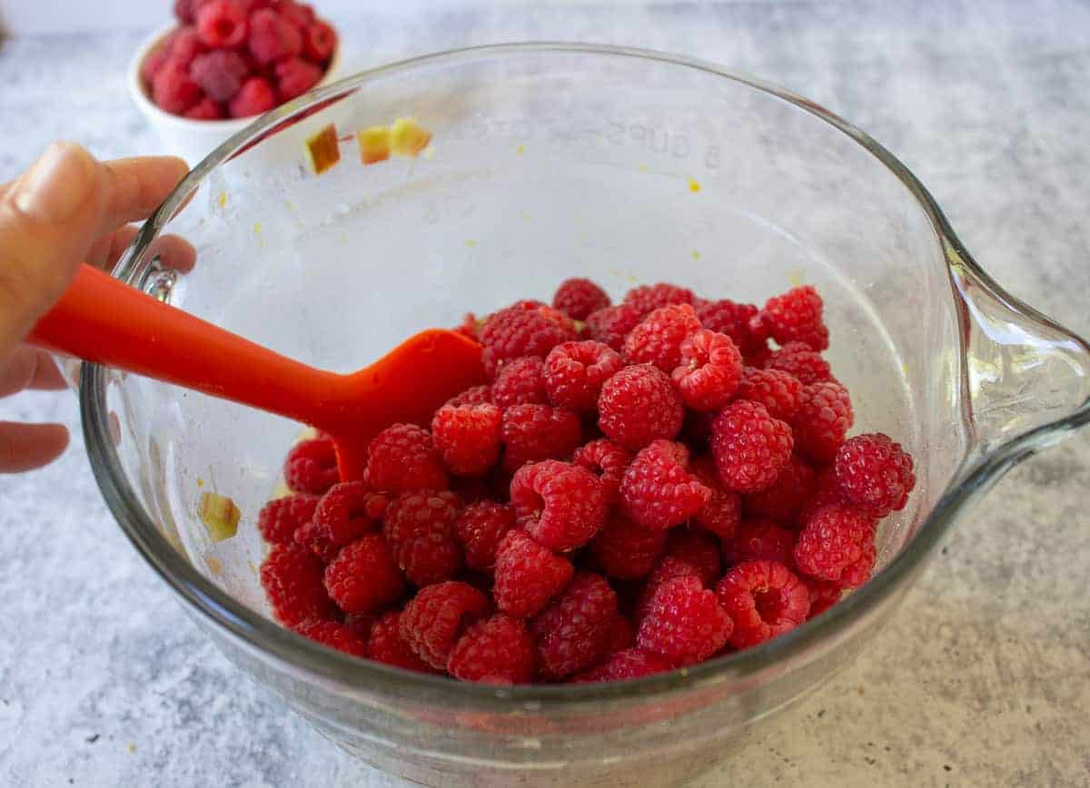 Fresh raspberries on top of a pie filling in a glass bowl.