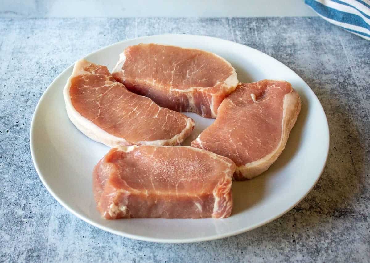 Uncooked boneless pork chops on a white plate.