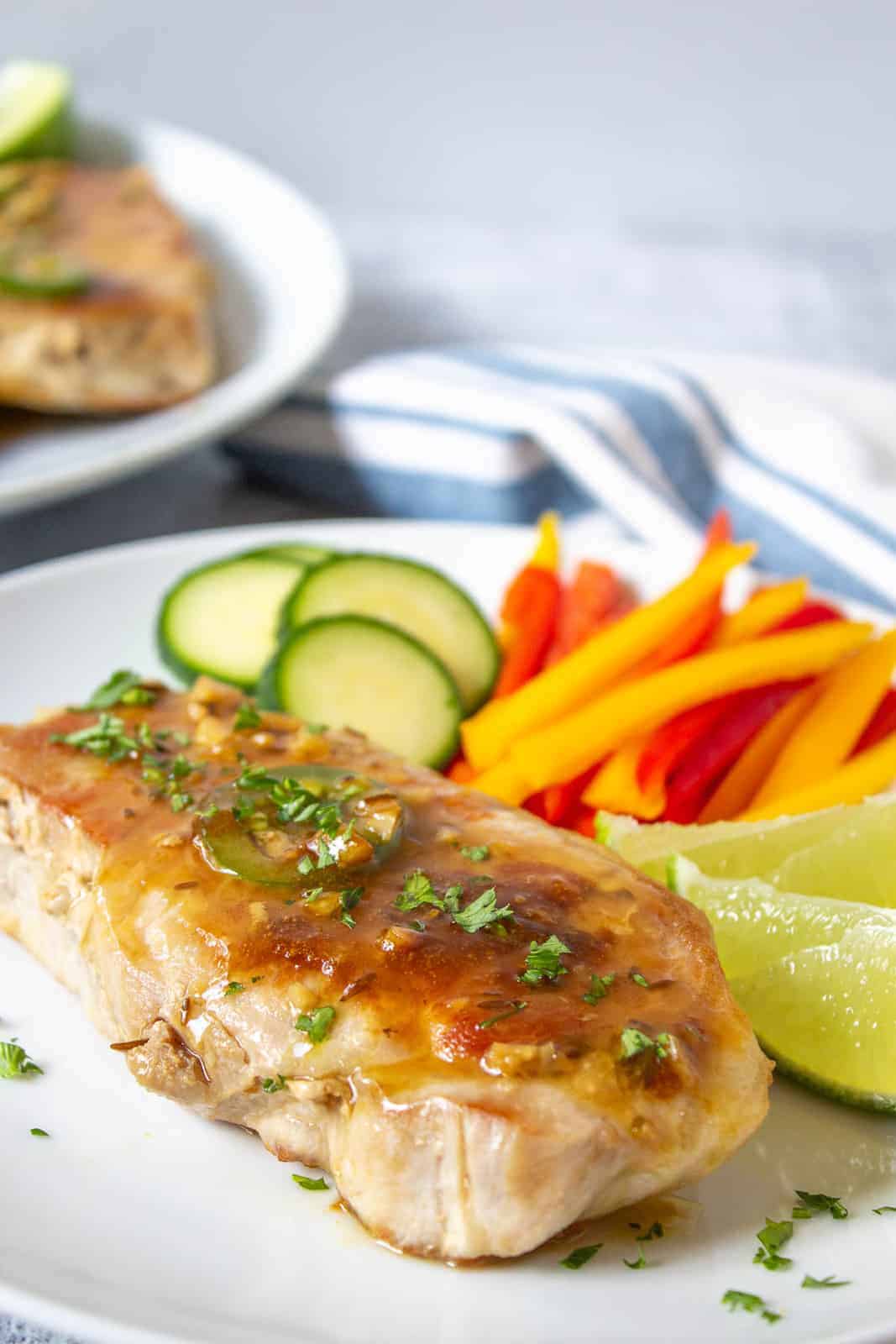 Tequila Lime Pork chops on a plate with fresh lime wedges and sliced vegetables.