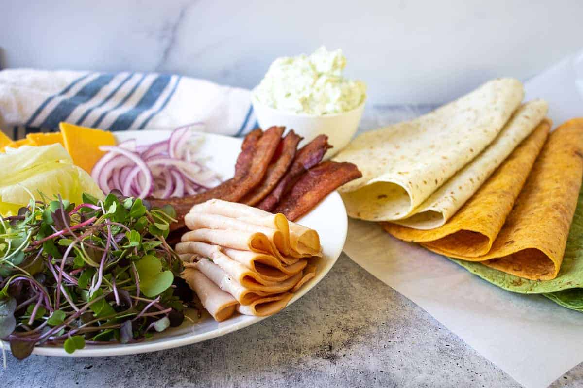 A plate filled with sandwich fillings and a variety of tortilla wraps.