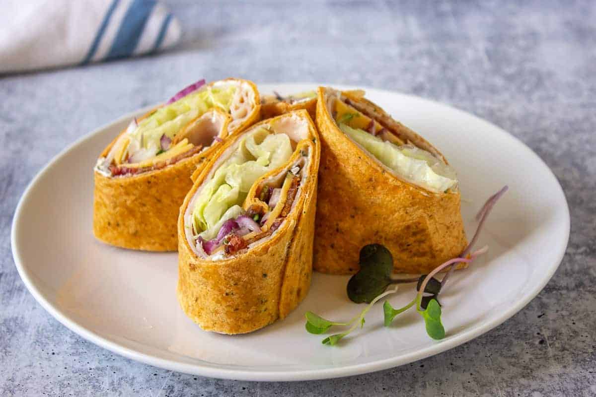 A turkey wrap cut into quarters standing upright on a white plate.