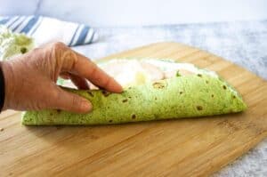 Rolling up a green tortilla wrap.