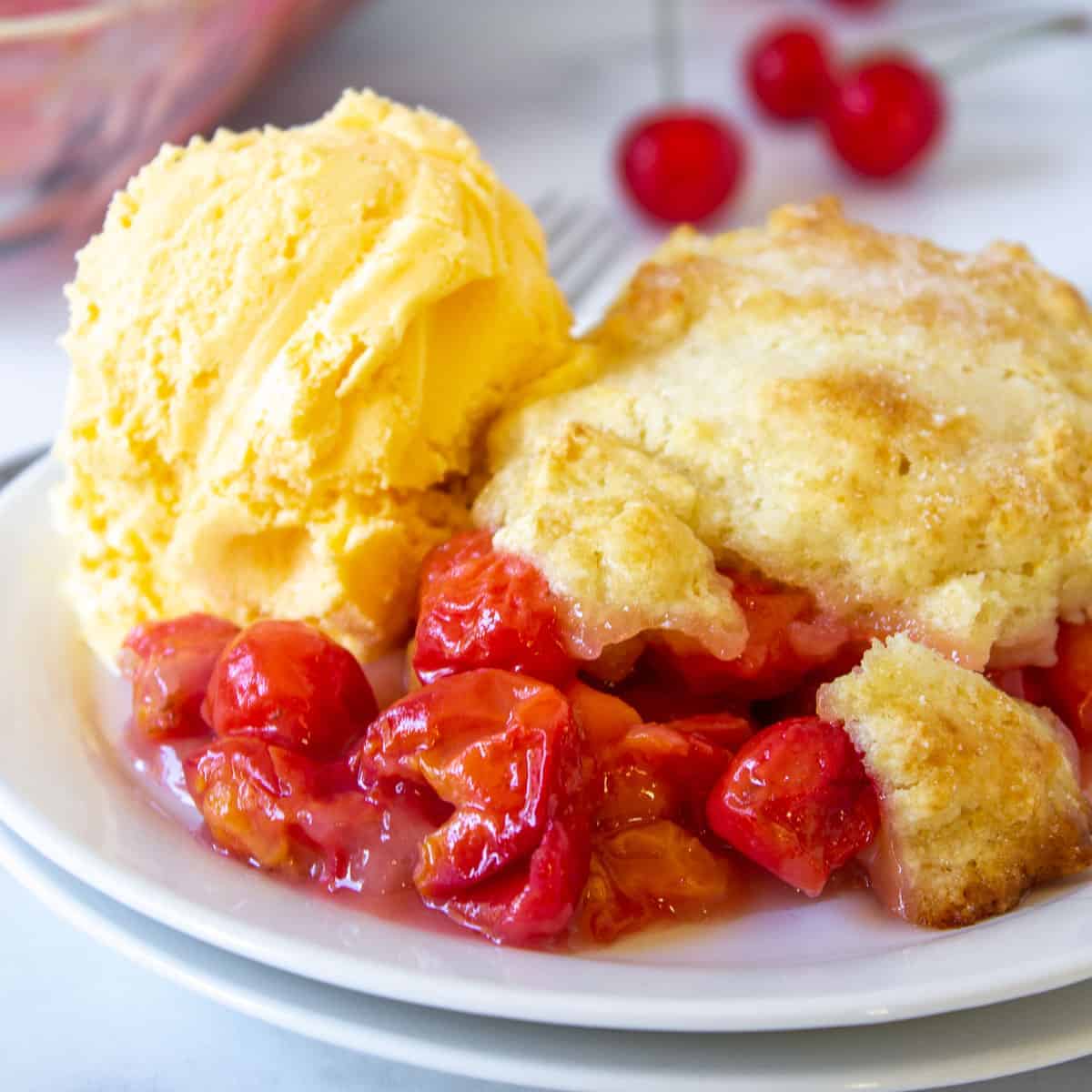 Cherry cobbler with red sour cherries topped with a scoop of vanilla ice cream.