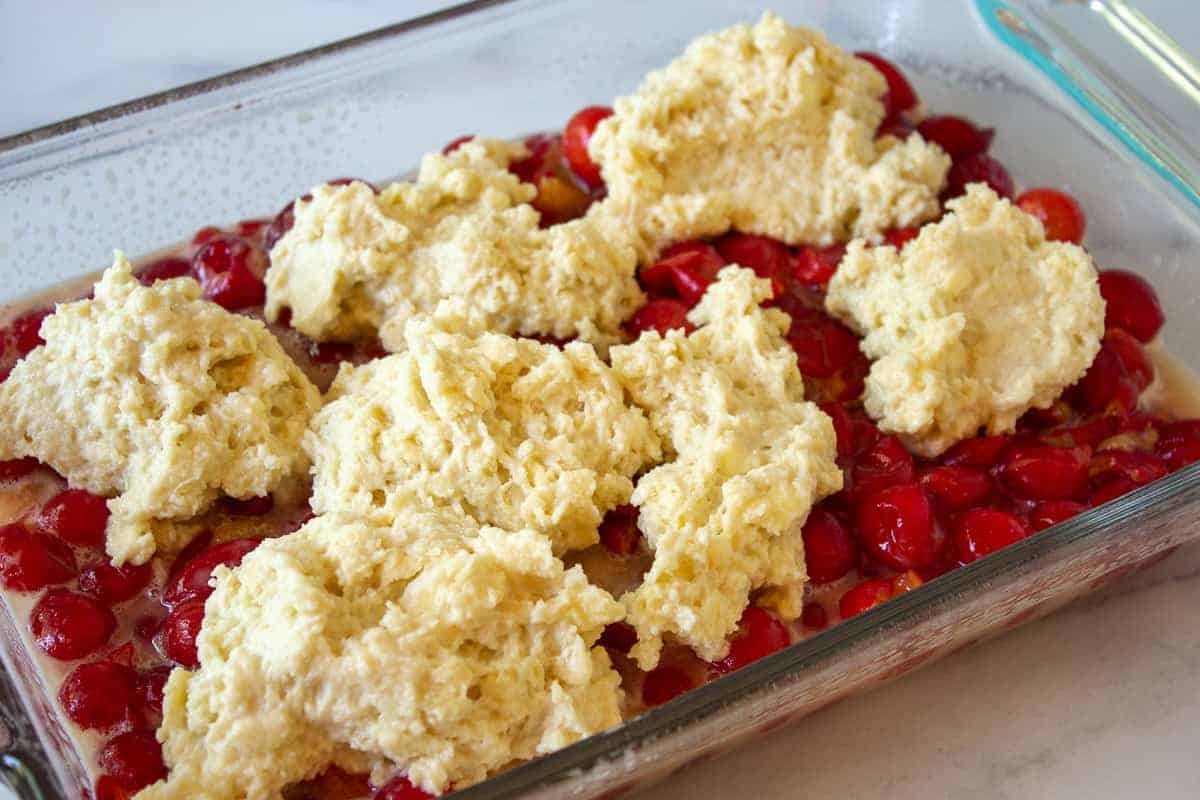 Biscuit dough on top of cherries in a baking dish.