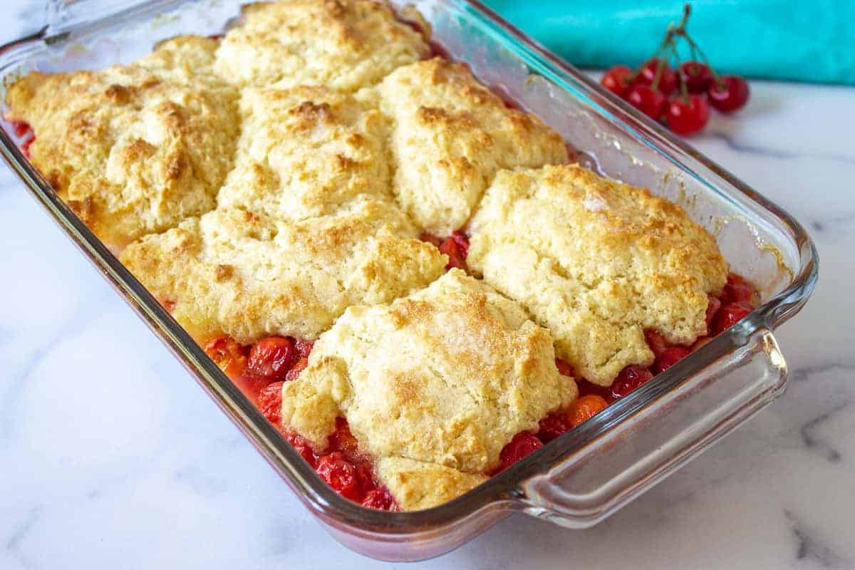 Baked cherry cobbler with a biscuit topping in a glass casserole dish.