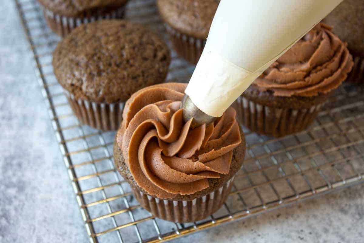Chocolate frosting being piped onto a chocolate cupcake. 