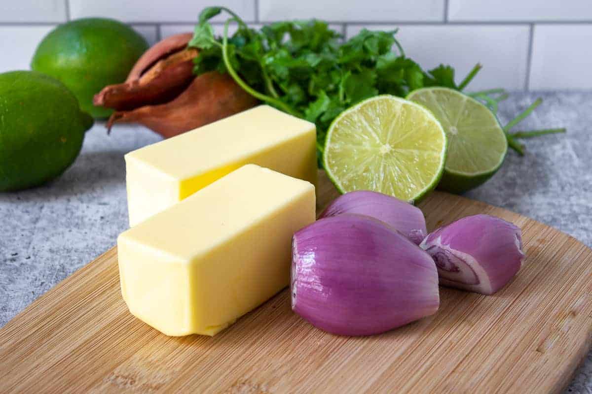 Sticks of butter, fresh shallots, limes and cilantro on a wooden board. 