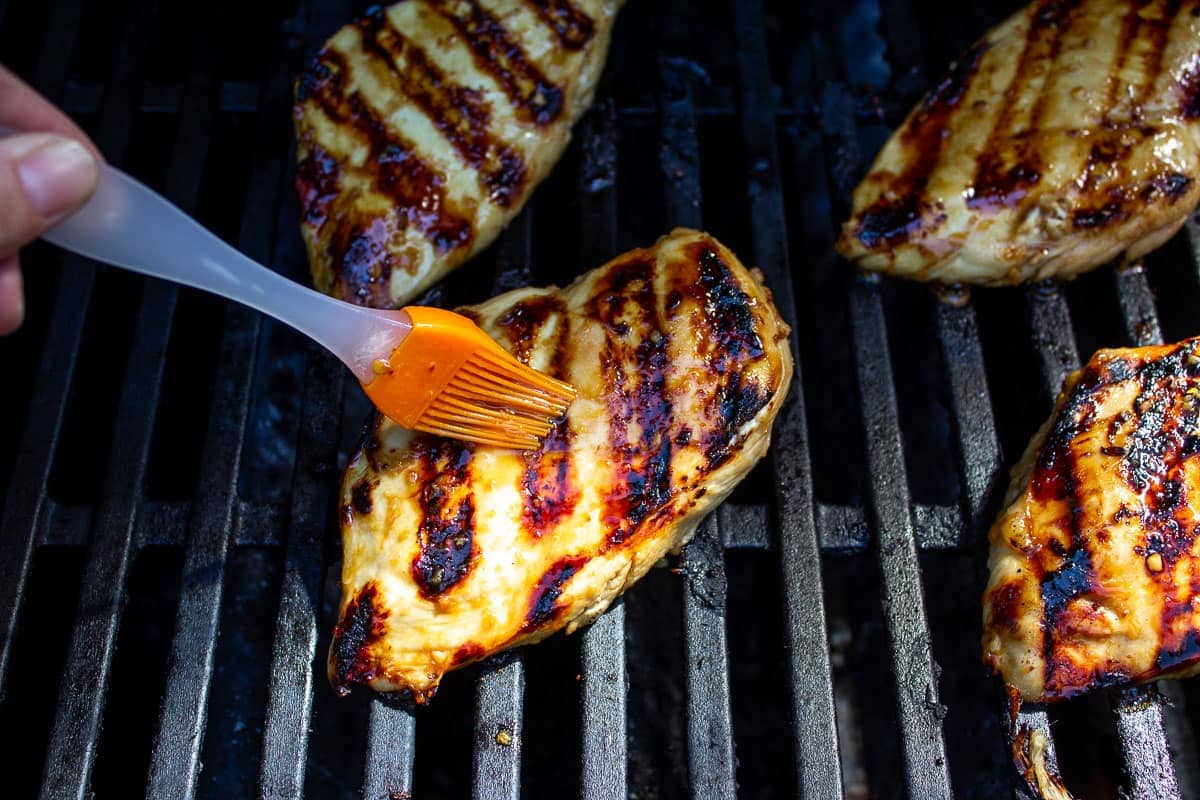 Chicken breasts on a grill being basted with a marinade.