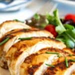 Sliced honey lemon chicken breast on a plate with a green salad.