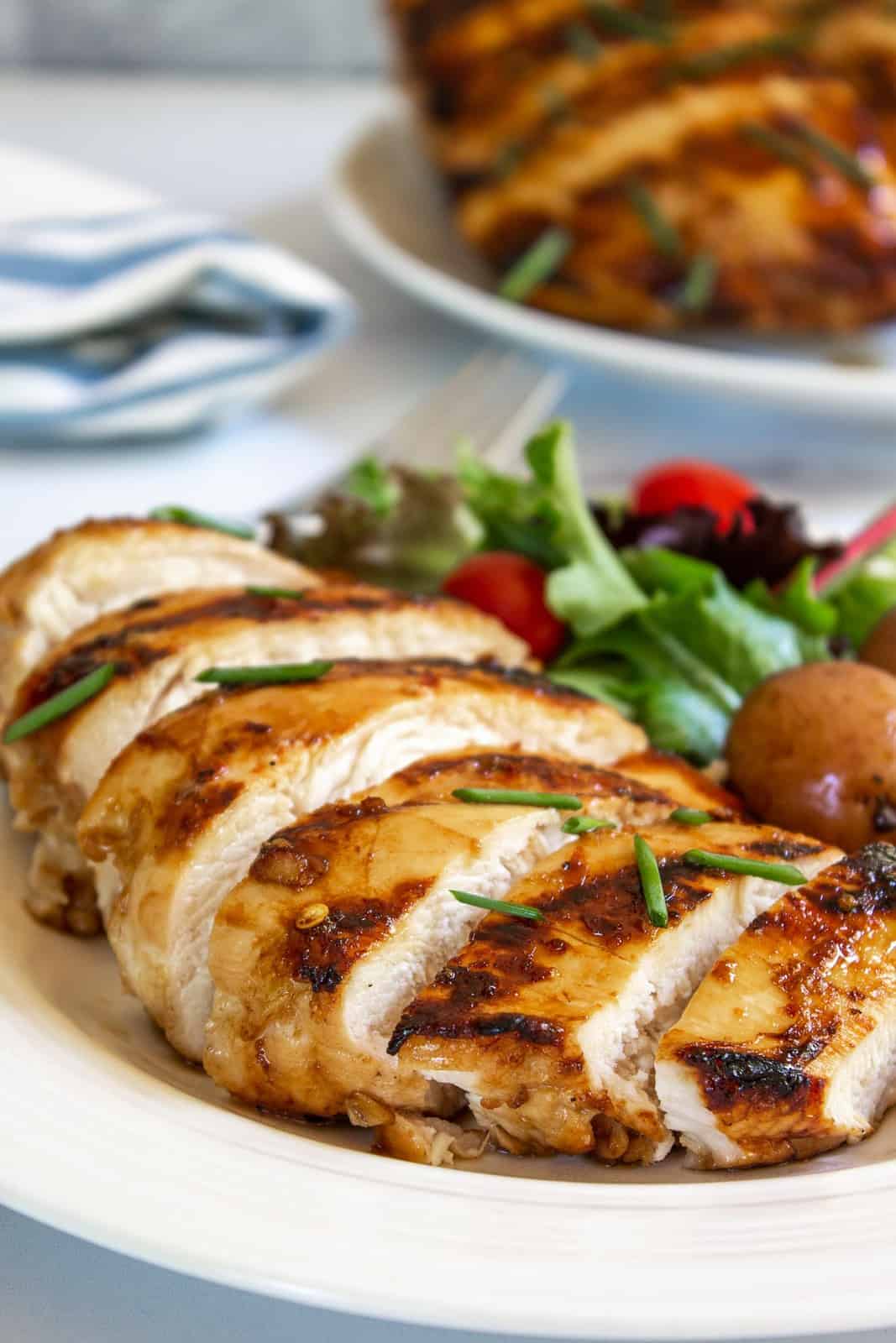 Sliced honey lemon chicken breast on a plate with a green salad.