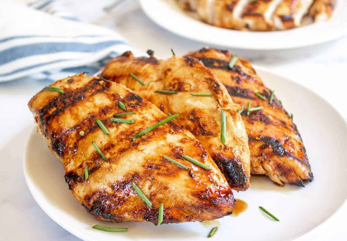 Grilled chicken breasts on a plate with fresh chopped chives.