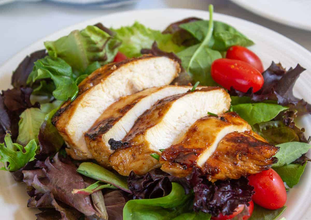 Sliced chicken breasts on top of a green salad.