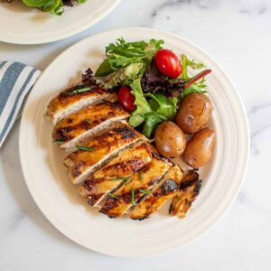 A plate with a sliced chicken breast, baby potatoes and a green salad.