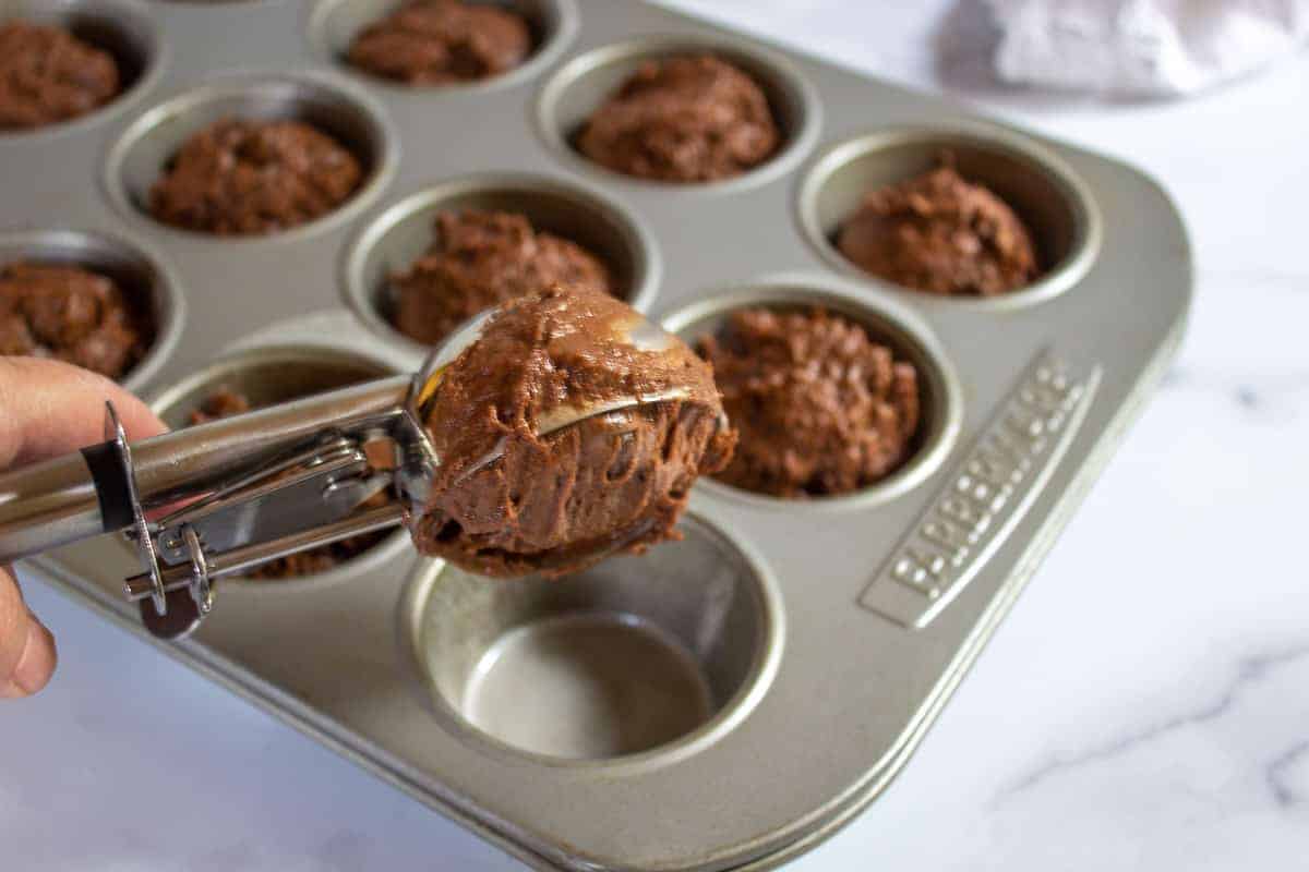 Scooping muffin batter into muffin tins.