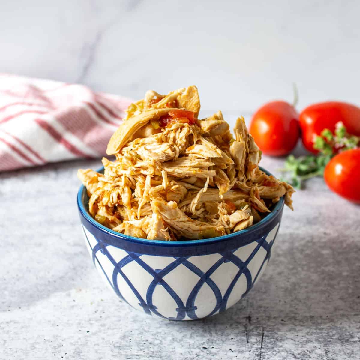 A blue and white bowl filled with shredded chicken and bits of tomatoes.