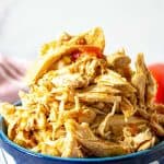 A bowl filled with shredded chicken and bits of tomatoes.