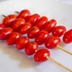 Skewered grilled cherry tomatoes on a white plate.