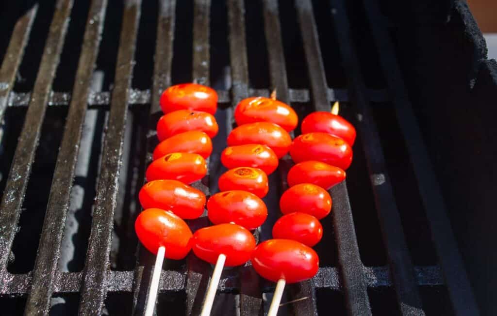 Cherry tomatoes cooking on a gas barbecue grill.