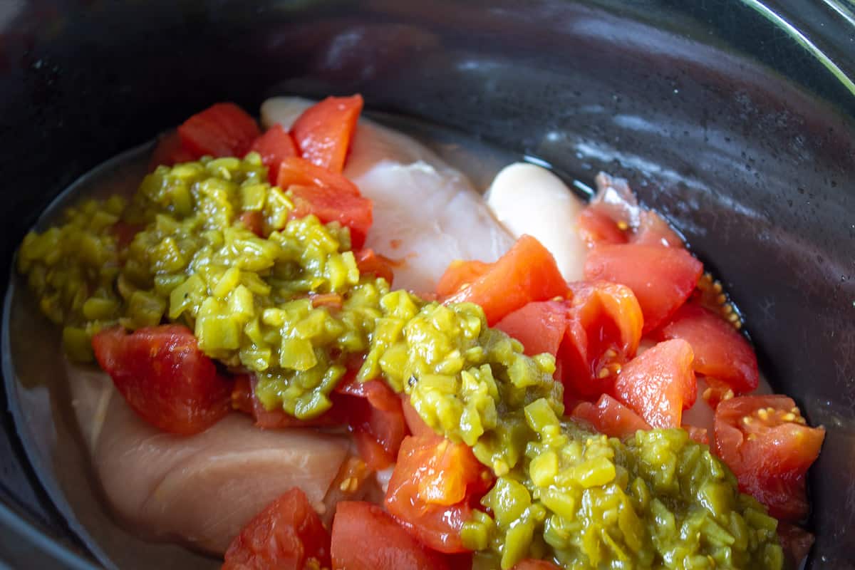 A crock pot with chicken, chopped tomatoes and green chilies. 