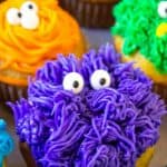 Purple, orange and blue frosted cupcakes with candy eyes.