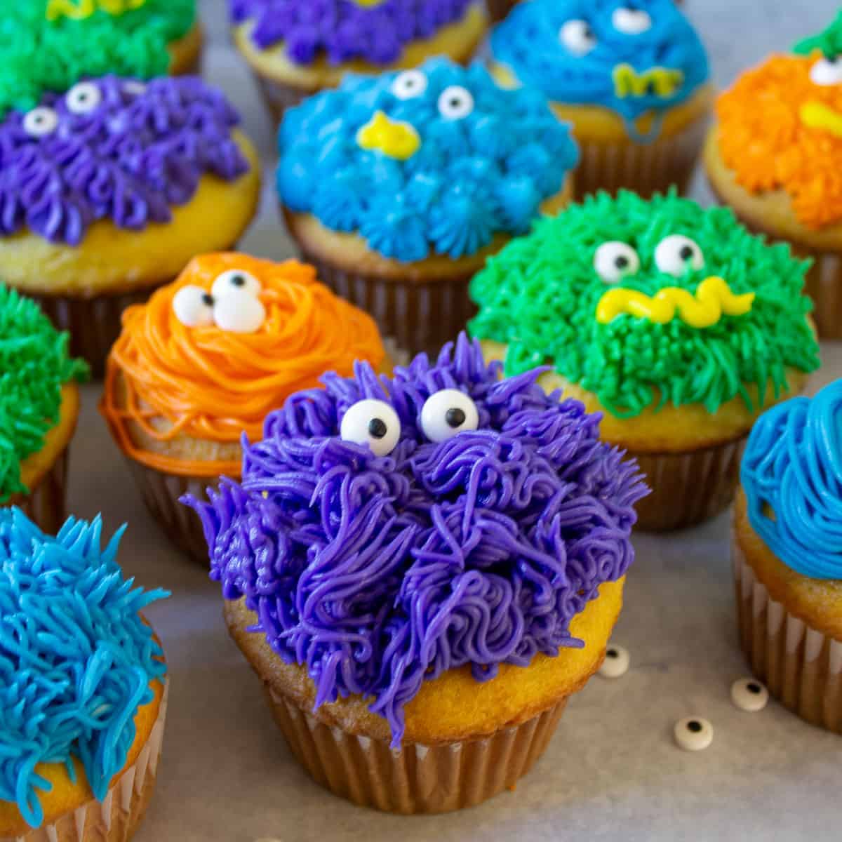 Colorful monster cupcakes with candy eyes arranged in a group.
