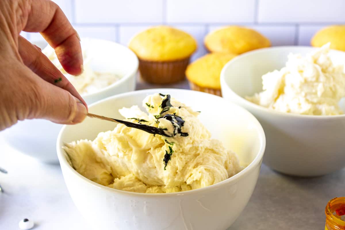 A bowl of frosting with a toothpick covered with a gel coloring. 