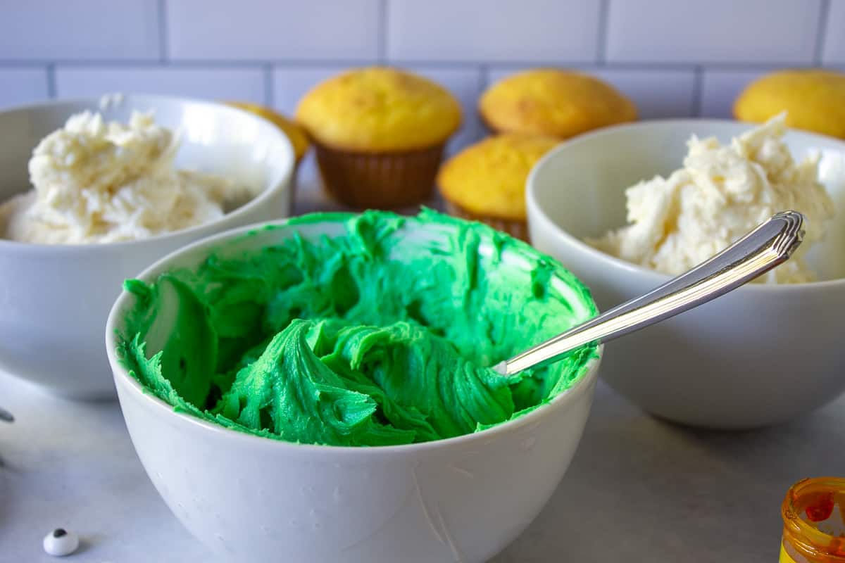 Green colored frosting in a white bowl.