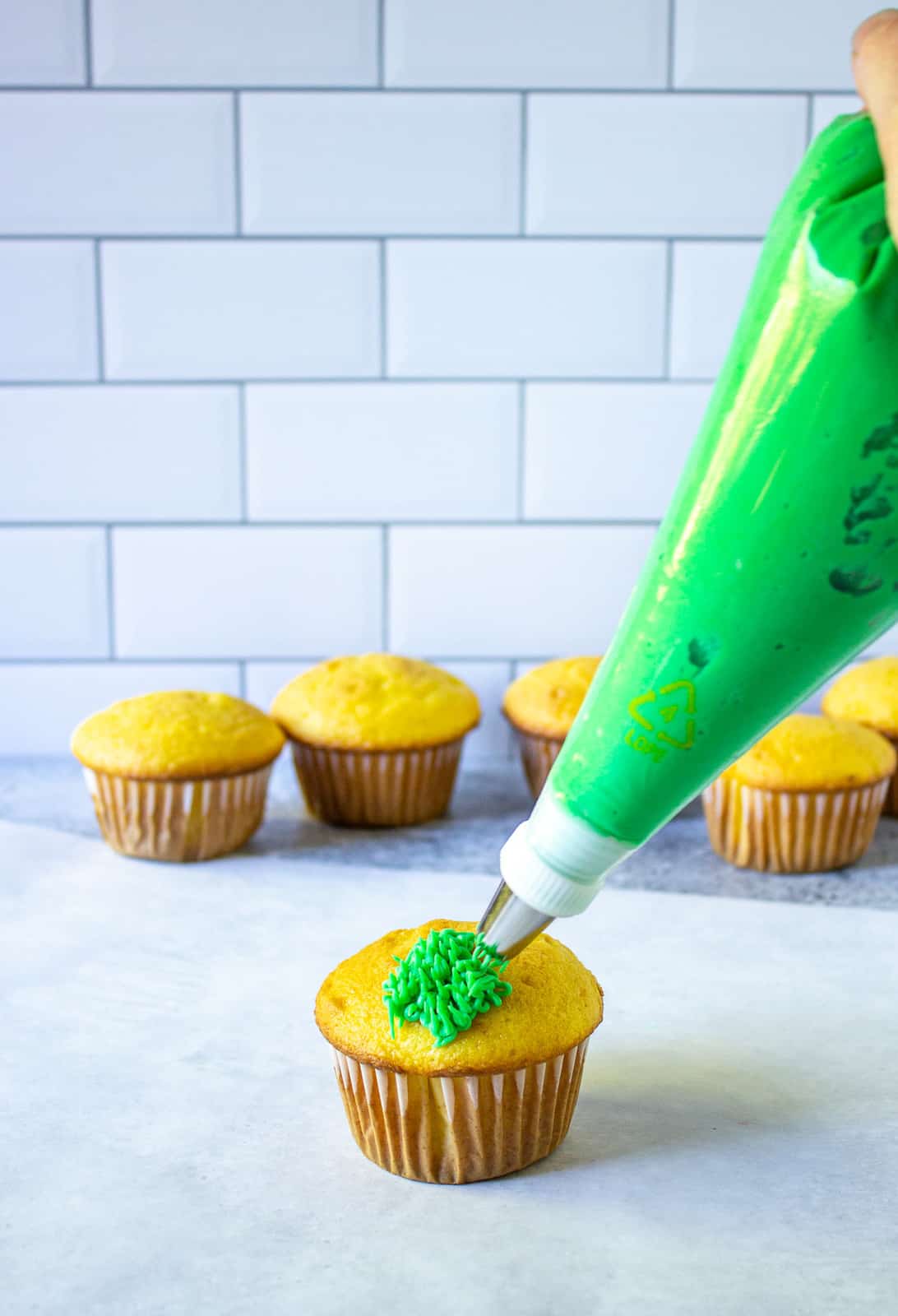 Adding green frosting to a cupcake.