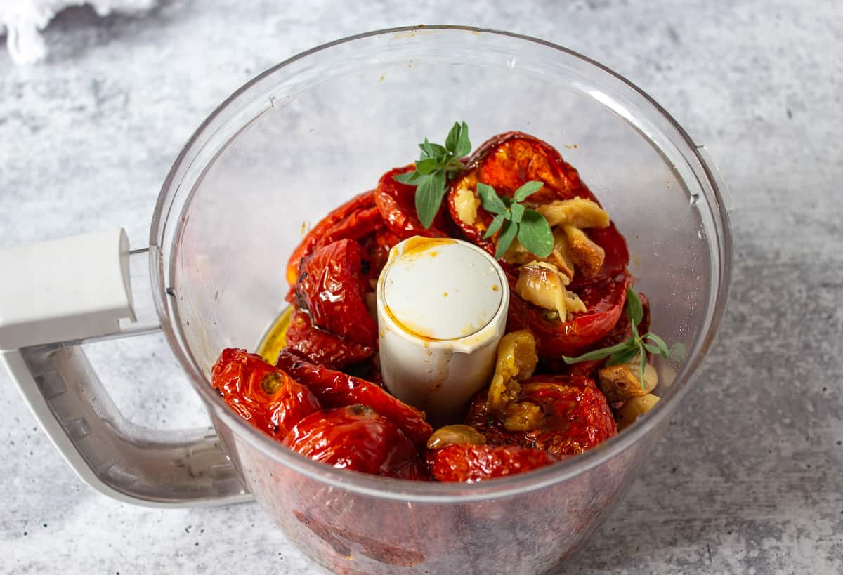 A food processor with tomatoes, garlic and fresh herbs.