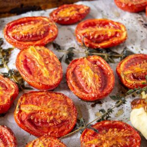 Oven roasted tomatoes with fresh herbs and garlic on a roasting pan.