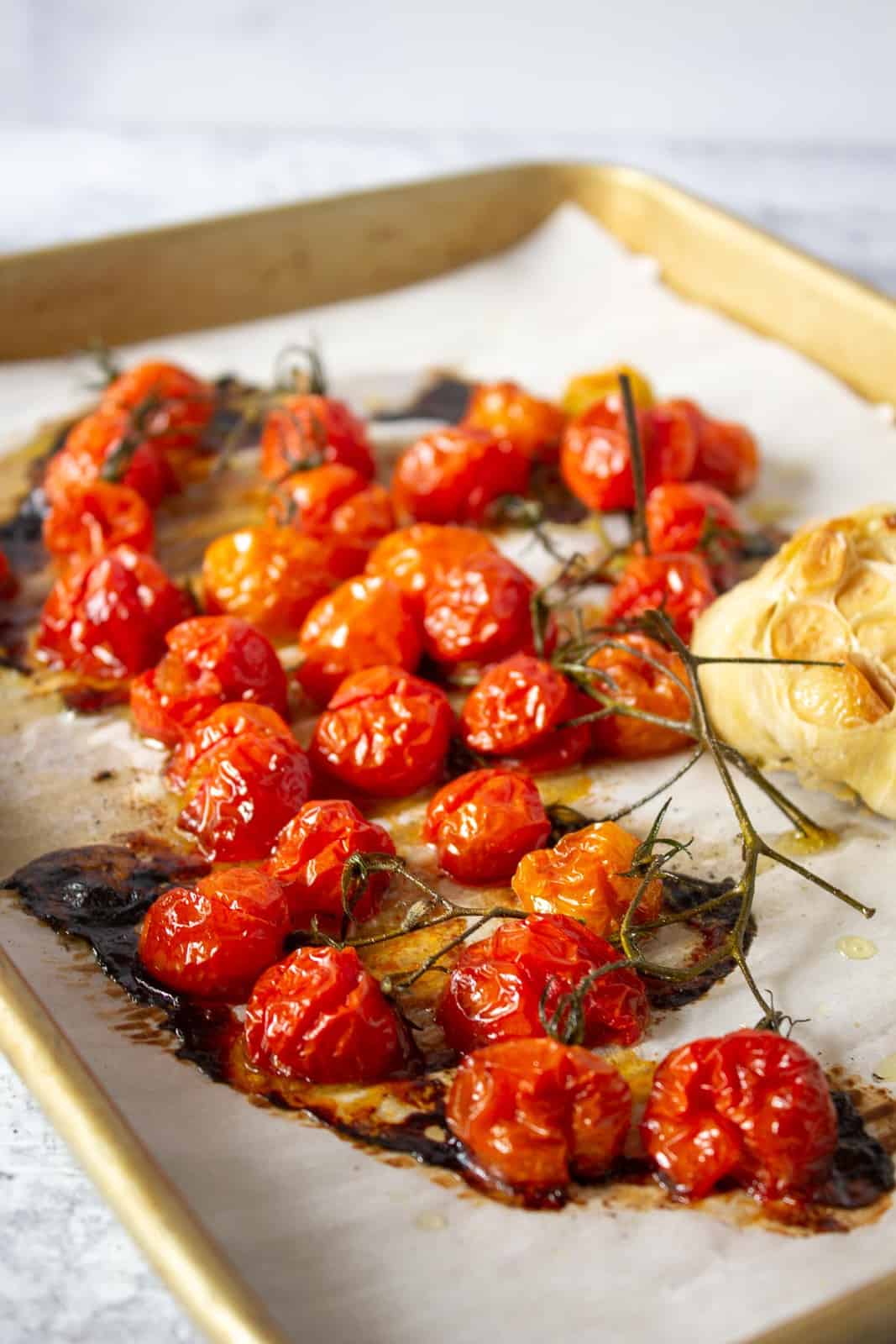 A baking sheet filled with oven roasted cherry tomatoes and roasted garlic.