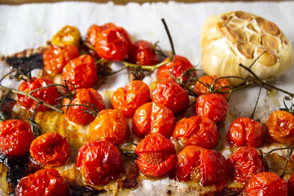 Roasted cherry tomatoes with roasted garlic on a baking sheet. 