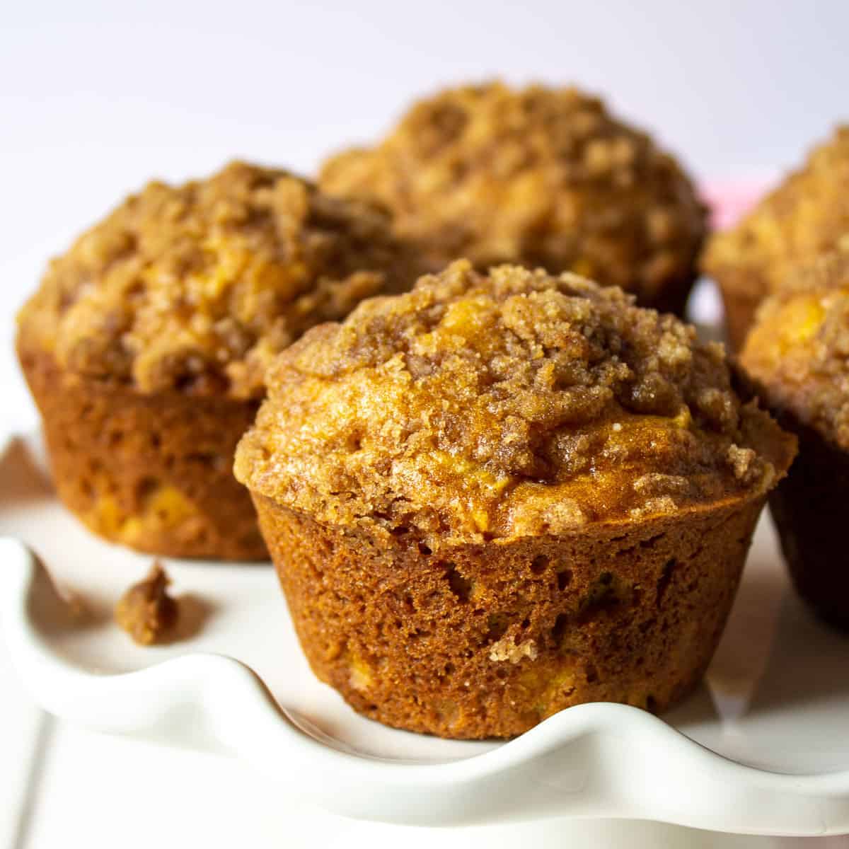 Pumpkin apple muffins with a streusel topping on a white cake stand.topping